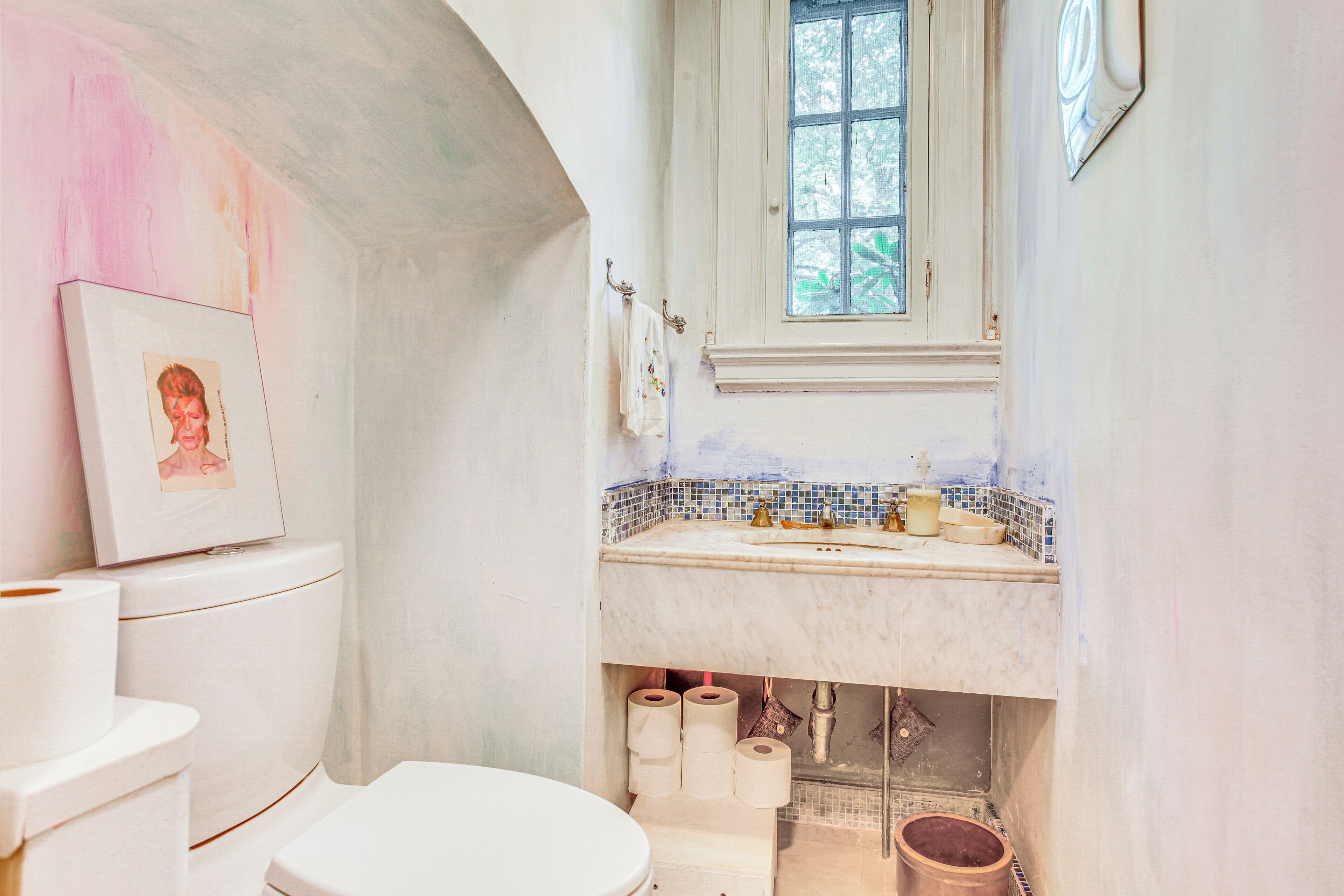 Une salle de bain avec des toilettes blanches, un lavabo orné de carreaux de mosaïque bleus et une fenêtre située au-dessus du lavabo.