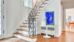A staircase with ornate metal railings and wooden steps, leading to a landing with a white radiator and a blue abstract painting. - Hudson Valley Estate on 4 Acres w/ Private Pool! (Nyack)