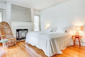 A bedroom with a large bed, a wicker chair, a fireplace, and a wall with drawings. - Hudson Valley Estate on 4 Acres w/ Private Pool! (Nyack)