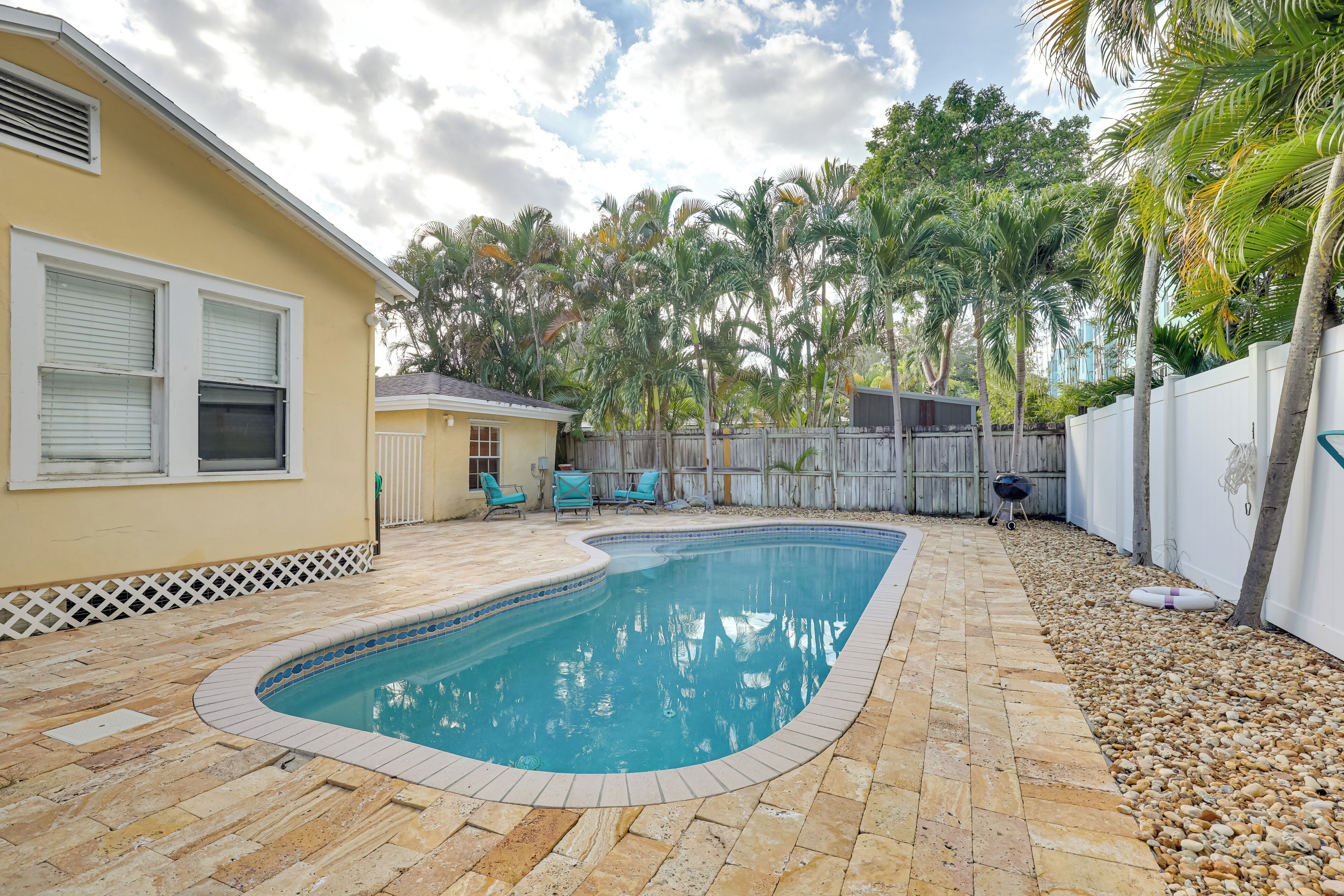Un jardin avec une piscine, des palmiers et une zone délimitée par une clôture.