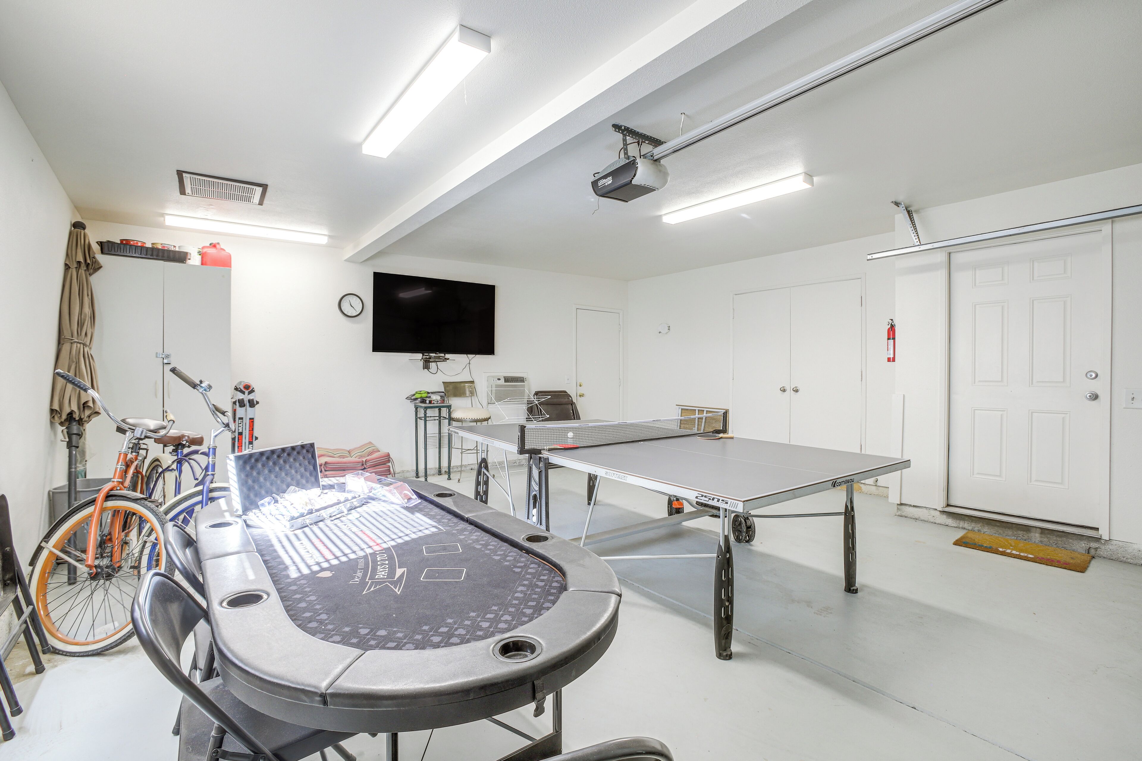 A room with a ping pong table, a bicycle, and a television mounted on the wall.