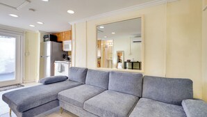 A modern living room with a grey sectional sofa, a large mirror, and a kitchen area with a refrigerator and microwave. - Detached Backyard Studio in Fort Lauderdale! (Fort Lauderdale)
