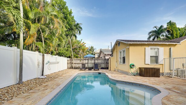A swimming pool with a tiled deck, surrounded by a white fence and palm trees. - Detached Backyard Studio in Fort Lauderdale! (Fort Lauderdale)