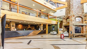 A spacious lobby with a reception desk, a stone fireplace, and a second-floor balcony with wooden railings. - Walk to Ski Lift: Resort Condo in Park City! (Park City)