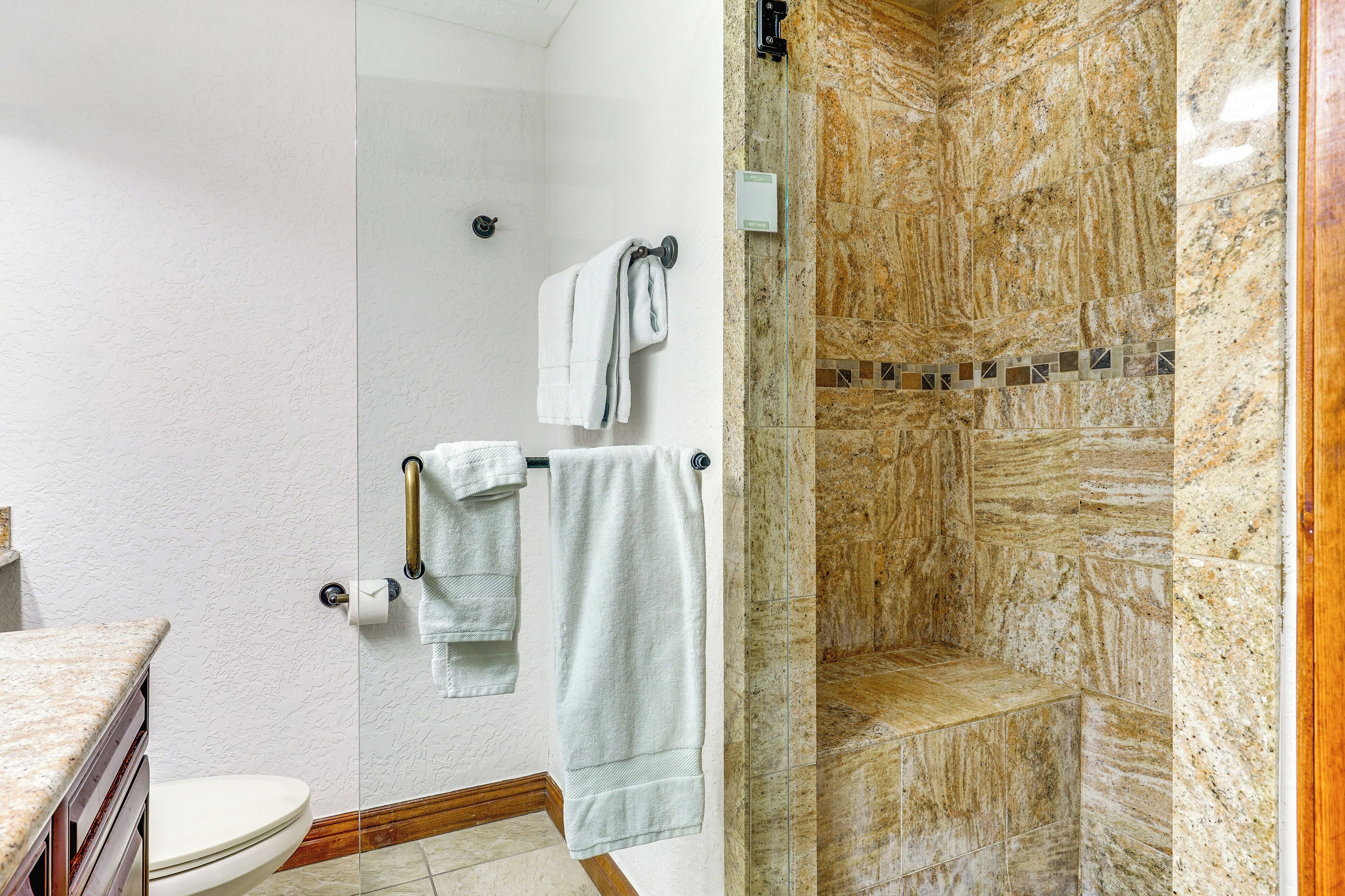 A bathroom with a glass-enclosed shower, marble walls, and a toilet.