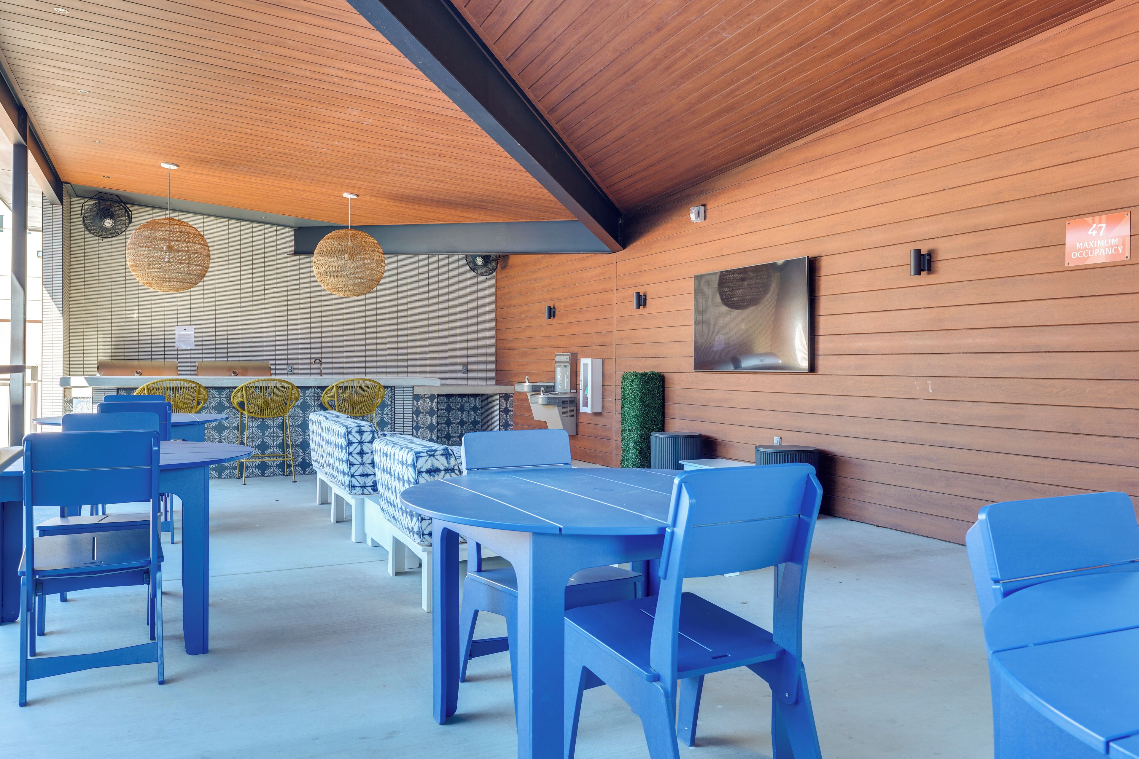 A modern interior with blue tables and chairs, wooden panel walls, and hanging wicker lamps.