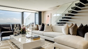 A modern living room with a white sofa, a coffee table, and a staircase with glass railings. - Top Urban Escape w Pool and Ocean View Villa Alexa (Cape Town)
