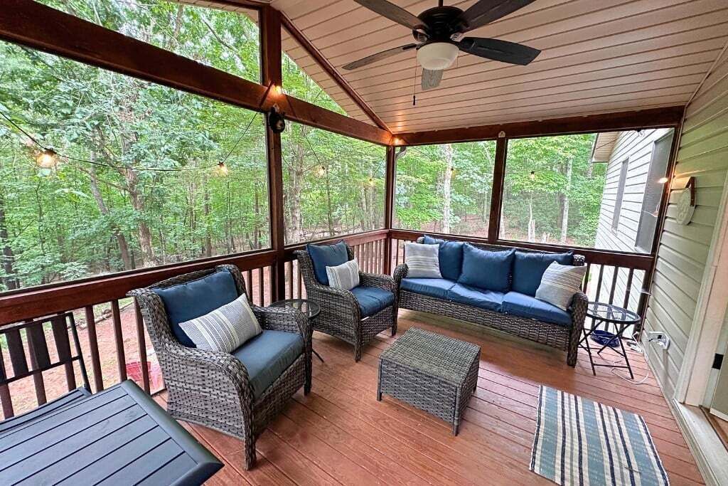 A covered porch with wicker furniture, a ceiling fan, and a view of the surrounding forest.