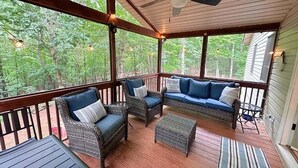 A covered porch with wicker furniture, a ceiling fan, and a view of the surrounding forest. - Modern Mountain at Rumbling Bald (Lake Lure)