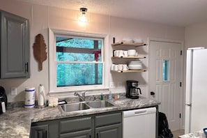Una cocina con ventana, un lavamanos, una cafetera y un refrigerador.