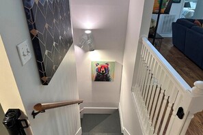 Una escalera con barandilla blanca, un aplique de pared y un cuadro de un perro colorido.
