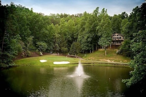 Un campo de golf con un estanque, una fuente y una casa al fondo.