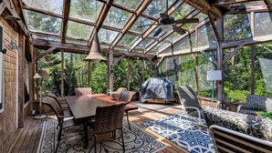 A spacious conservatory with a wooden table and chairs, a grill, and patterned rugs. - Spacious Home With Private Heated Pool (2389) (Wellfleet)
