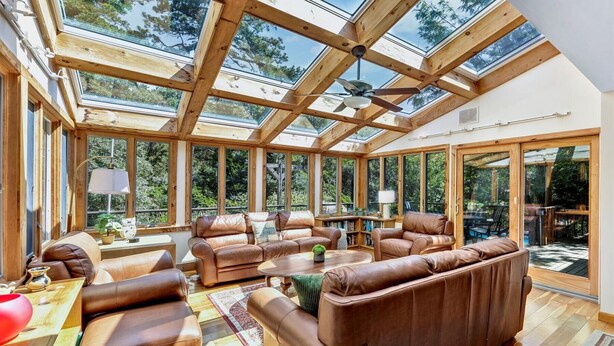 A sunroom with a high ceiling, large windows, and leather furniture. - Spacious Home With Private Heated Pool (2389) (Wellfleet)