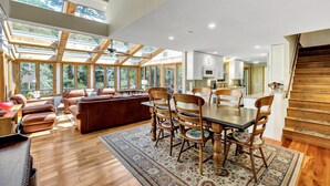 A spacious living area with a wooden dining table, leather sofa, and a large windowed wall. - Spacious Home With Private Heated Pool (2389) (Wellfleet)
