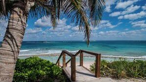 Una terraza de madera que da a una playa con agua turquesa cristalina y una palmera.