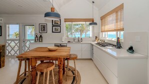 Una cocina moderna con una mesa de madera, luces colgantes y vistas al océano.