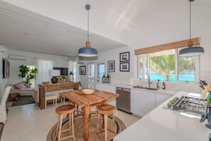 Et moderne køkken med en central ø, et spiseområde med et træbord, og havudsigt gennem store vinduer.