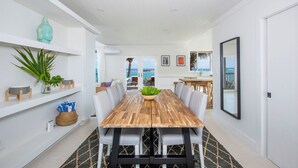 Un moderno comedor con una mesa de madera, sillas tapizadas en gris y vistas al océano a través de amplias ventanas.