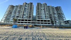 Um edifício residencial alto, com várias sacadas e vista para a praia.