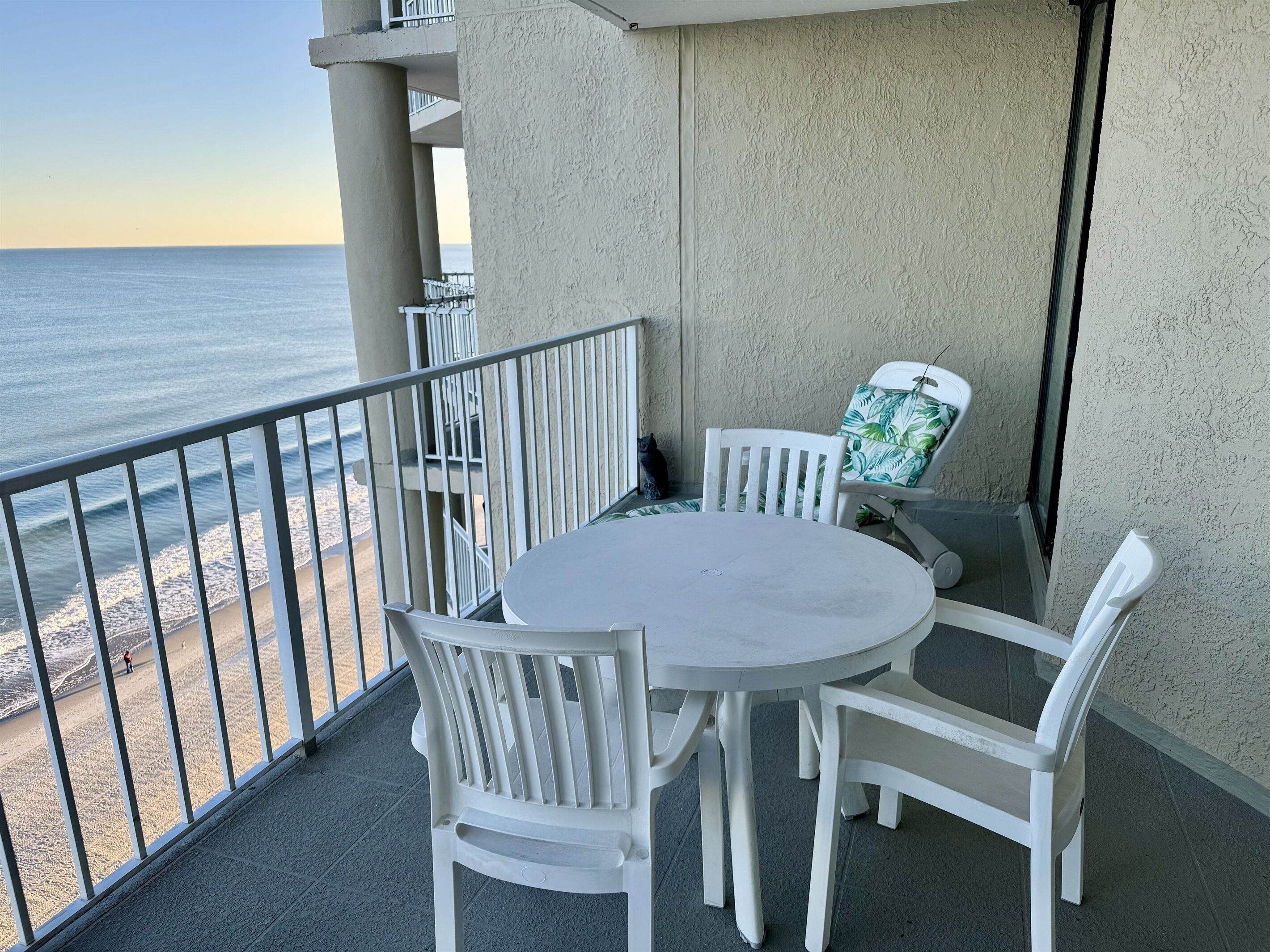 A balcony with a round table and white chairs, overlooking a beach.