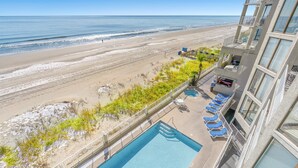 Um hotel com piscina, vista para a praia e varanda com espreguiçadeiras.
