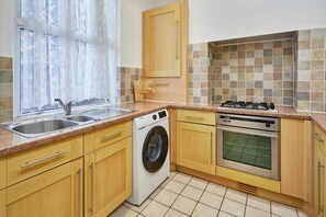 A kitchen with wooden cabinets, a washing machine, an oven, and a sink. - Host Stay Milford Road (Birmingham)