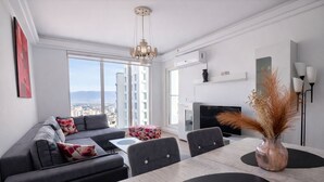 Una sala de estar moderna con sofá, mesa de comedor y sillas. Hay un televisor y un jarrón decorativo con plantas secas.