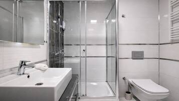 A modern bathroom with a glass-enclosed shower, a white sink, and a toilet.