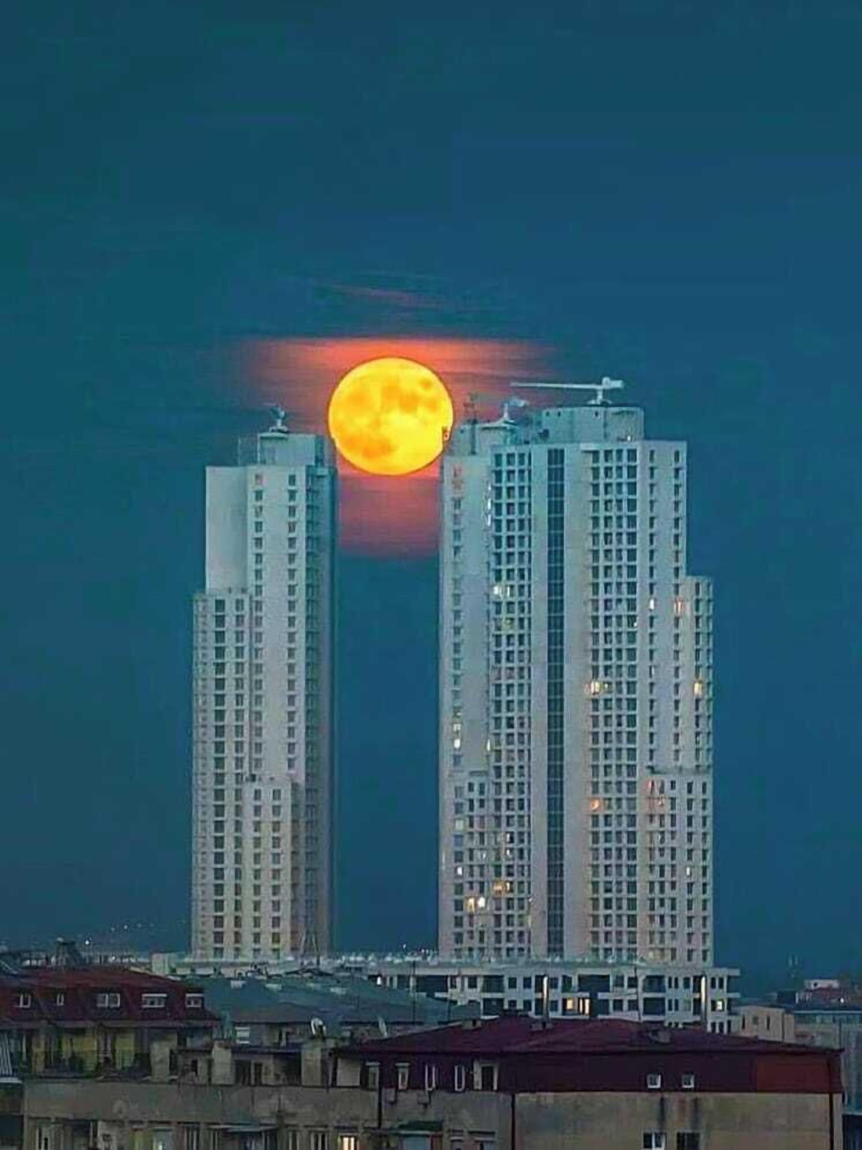 Due grattacieli con una grande luna nel cielo.