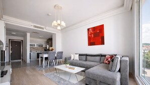 Una sala de estar moderna con un sofá gris, una mesa de centro blanca y una zona de comedor con sillas.