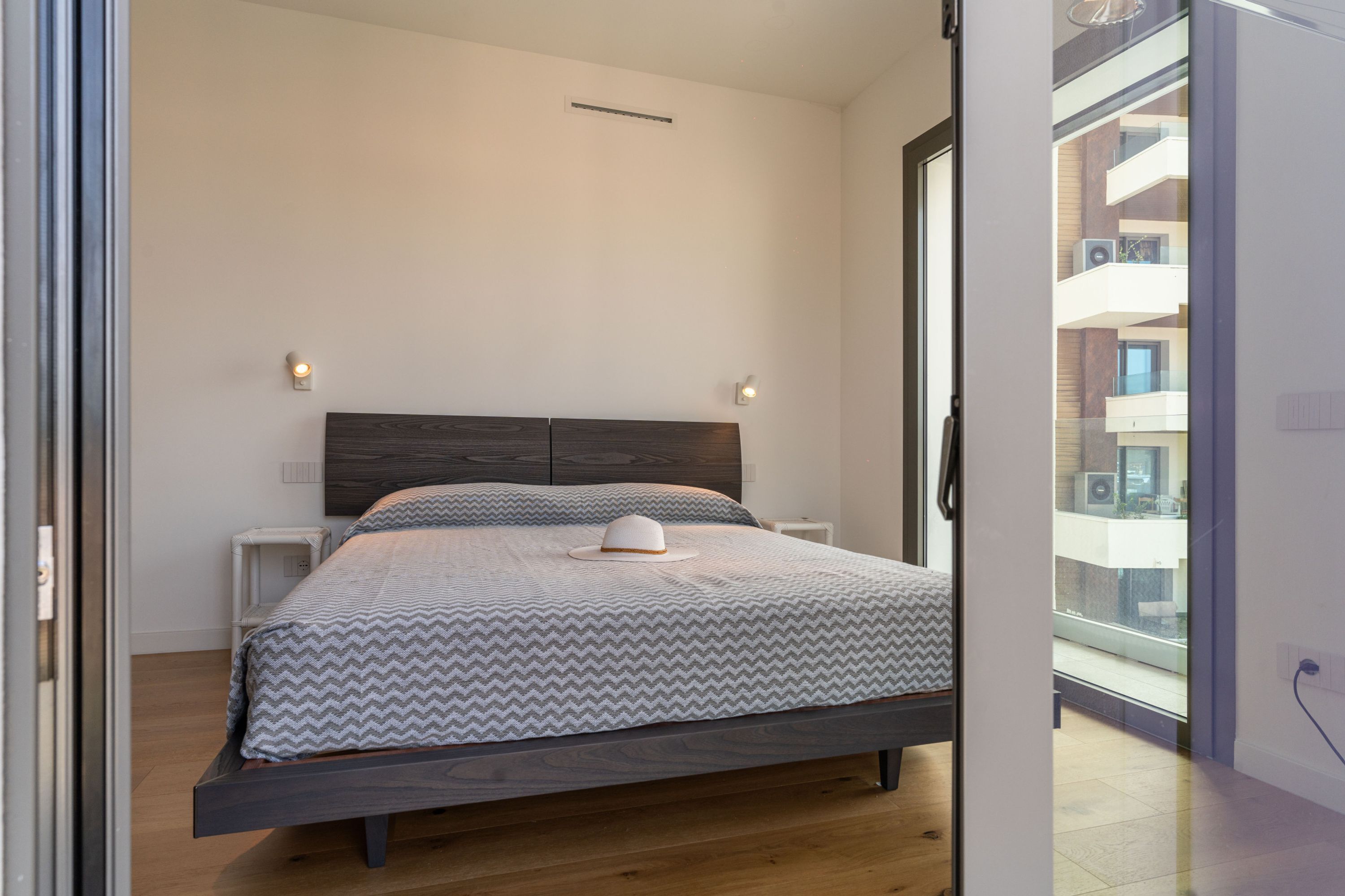 Een moderne slaapkamer met een bed, nachtkastjes en uitzicht op het balkon.