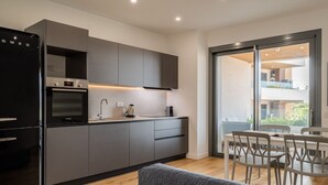 A modern kitchen with grey cabinets, a black refrigerator, and a dining area with a table and chairs. - Loft 4 by Wonderful Italy (Olbia)