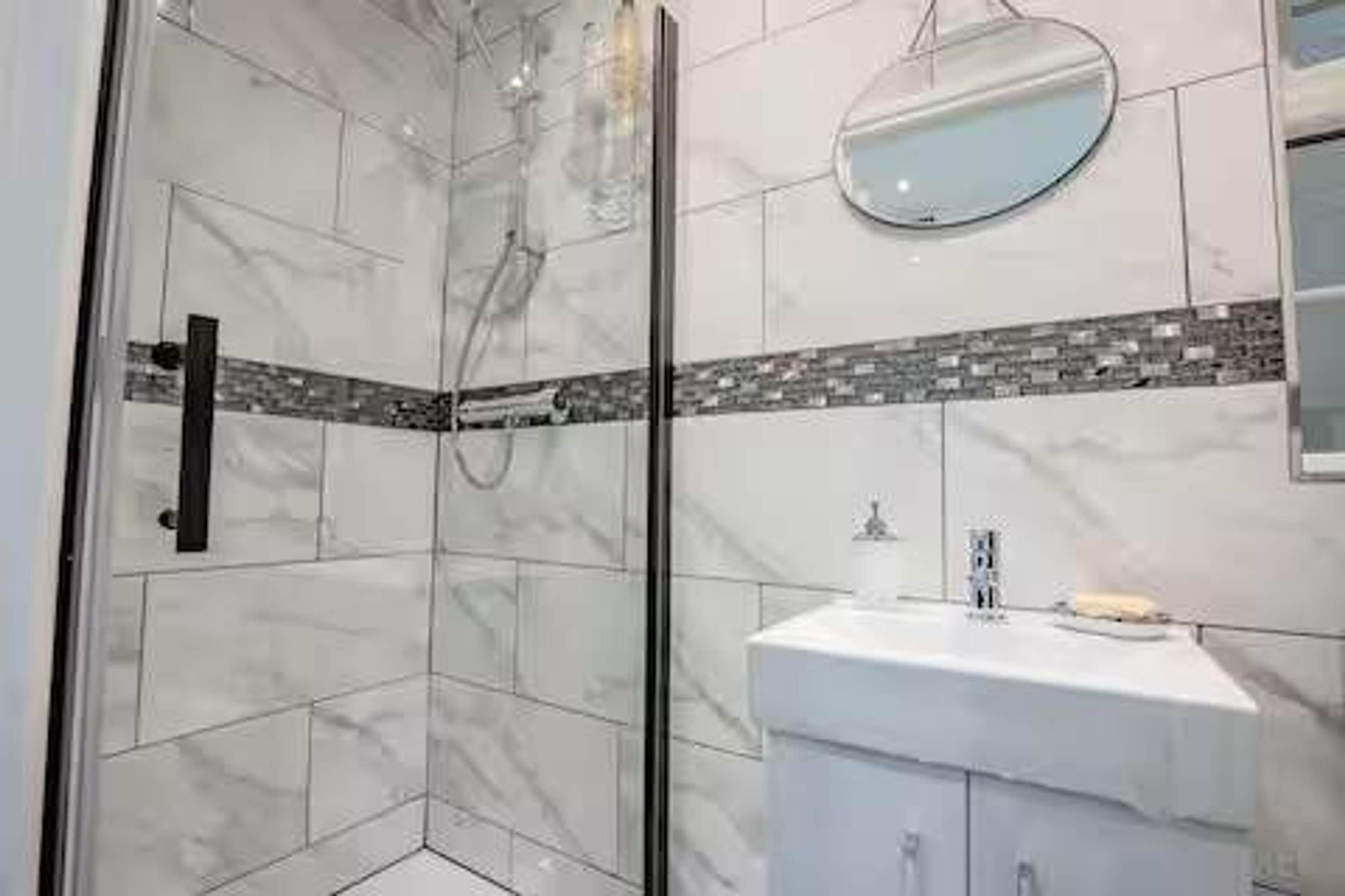 A modern bathroom with a glass shower enclosure, a white sink, and a mirror.