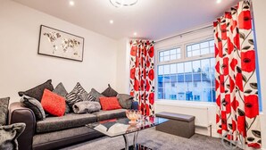 A modern living room with a sofa, cushions, a glass coffee table, and red and white patterned curtains. - Host Stay Broadland House (Southampton)