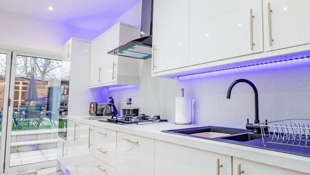 A modern kitchen with white cabinets, a black faucet, and under-cabinet lighting. - Host Stay Broadland House (Southampton)