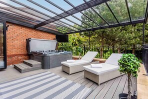 A covered outdoor deck with a hot tub, lounge chairs, and a television. - Host Stay The Grove (Hartlepool)