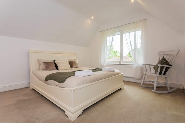 A bedroom with a large bed, a rocking chair, and a window with curtains.