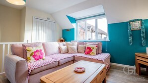 Una sala de estar acogedora con un sofá modular, una mesa de centro de madera y un ventanal con vistas a casas.