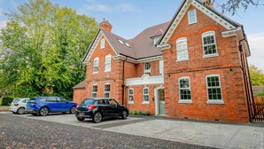 A red brick building with a gabled roof and white trim. There are two cars parked in front.