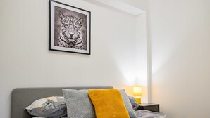 A neatly made bed with a patterned pillow, a framed picture on the wall, and a bedside table with a lamp.