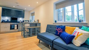 A modern kitchen with dark cabinets, a dining area with a table and chairs, and a sofa with colorful cushions.