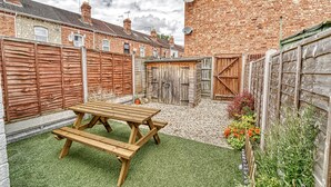 A backyard with a wooden picnic table, a brick building, and a brick wall. - Host Stay Southfield Residence (Worcester)