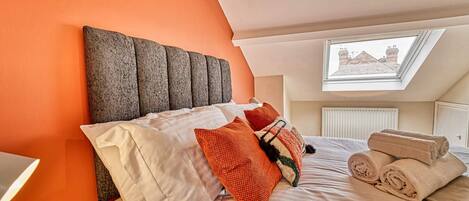 A bedroom with a sloped ceiling, a large window, and a bed with multiple pillows and rolled towels.