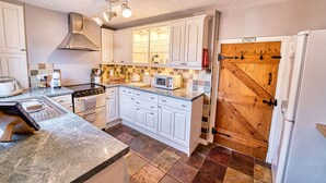 Une cuisine avec des armoires blanches, une cuisinière, un four à micro-ondes et une porte en bois.