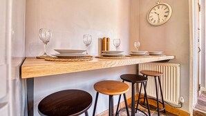 Un coin repas avec une table en bois, quatre tabourets et une horloge murale.