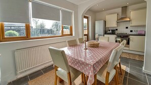 A dining area with a table set for six, a kitchen in the background, and a view of the outside. - Host Stay Severn Swans House (Worcester)