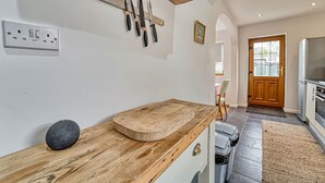 A kitchen with a wooden countertop, a cutting board, and a knife rack. There is a door leading to another room and a refrigerator in the background. - Host Stay Severn Swans House (Worcester)