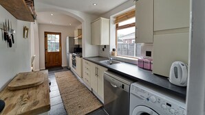 A modern kitchen with white cabinets, a dishwasher, and a sink. There is a wooden cutting board and a rug on the floor. - Host Stay Severn Swans House (Worcester)