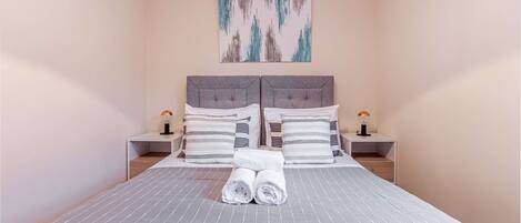 A neatly made bed with striped bedding, two bedside tables with lamps, and a painting on the wall.
